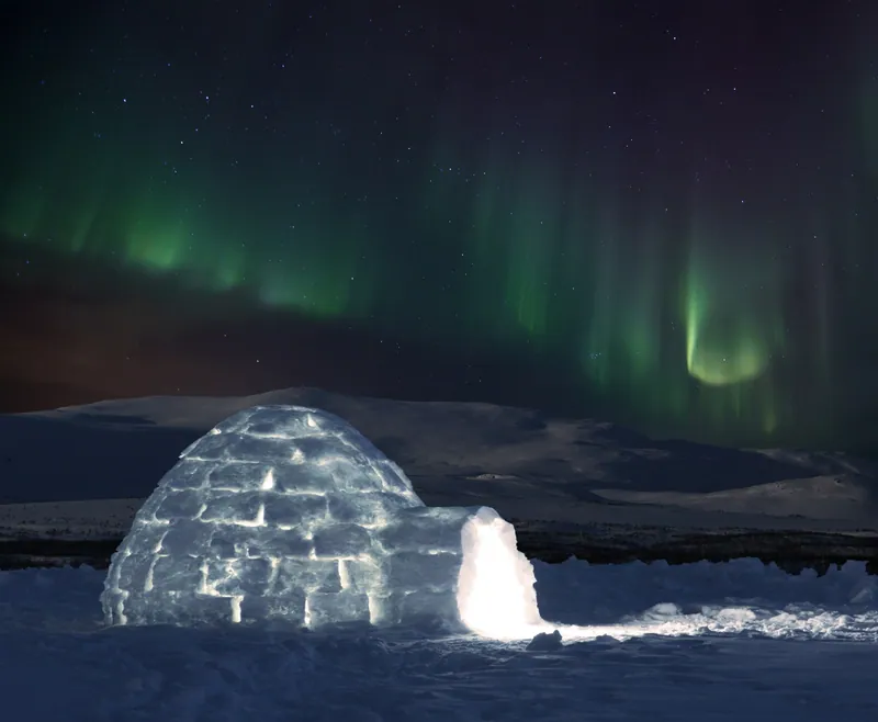 Glowing igloo under dramatic teal and blue aurora curtains